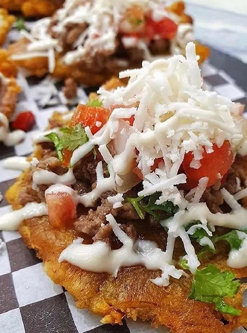 Tostón de plátano verde con carne, queso blanco rallado y tomate